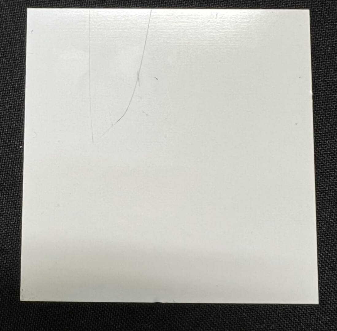 A white square tile sitting on top of a black floor.